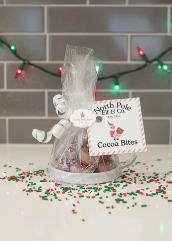 Gift bag of Cocoa Bites with a tag on a surface with festive decorations.