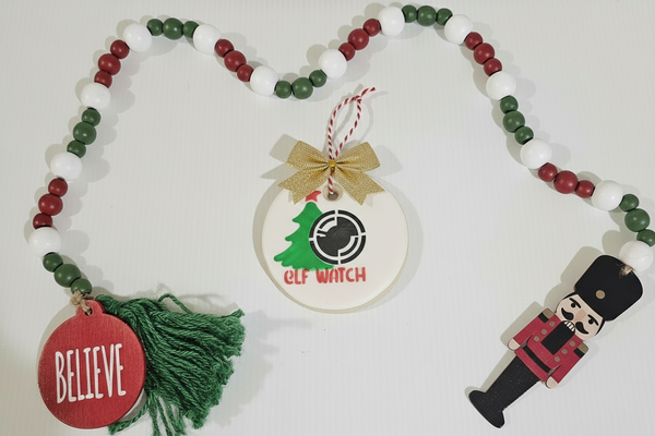 Decorative Christmas ornament with beads, a tag, and a nutcracker figure on a white background.